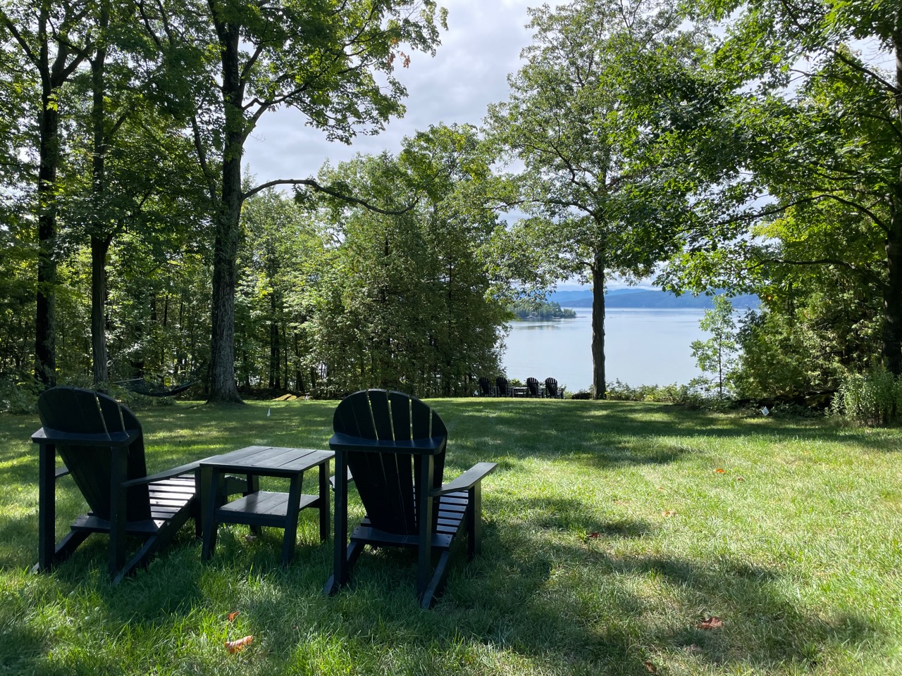 A lakefront lawn with adirondack chairs looks green after NH organic lawn care services